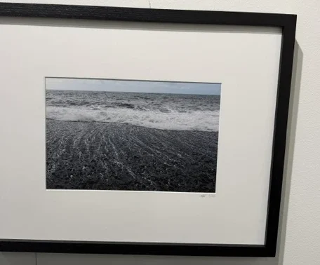 Rough Basis, Soft Being by Mariana de la Vega, a framed photograph of waves washing across a dark textured shore.