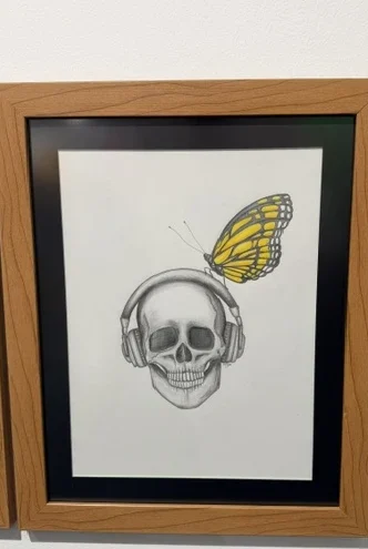 Cone Skull by Paola Fuentes, a framed pencil drawing of a skull wearing headphones with a monarch butterfly perched above.
