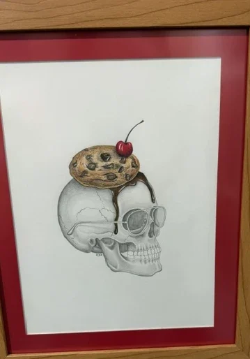Cookie Skull by Paola Fuentes, a framed pencil drawing of a skull topped with a chocolate-chip cookie and cherry.