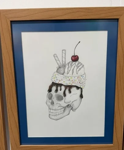The Intabee by Paola Fuentes, a framed pencil drawing of a skull topped with a decorated ice cream dessert and cherry.